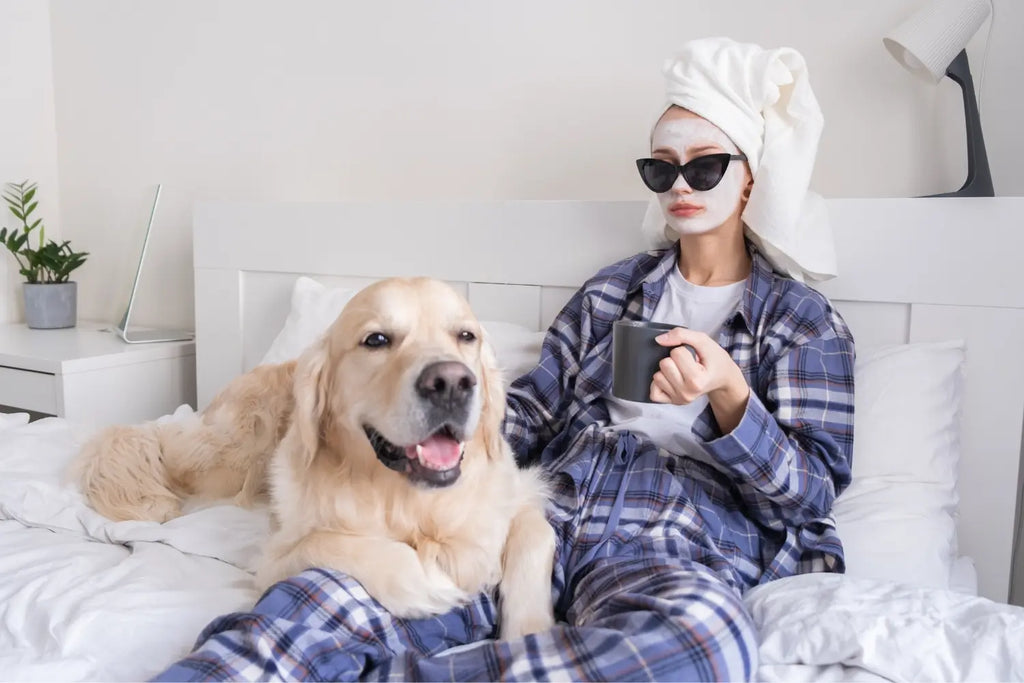 Woman with towel wrapped on her head, sitting on bed with her golden retriever dog.