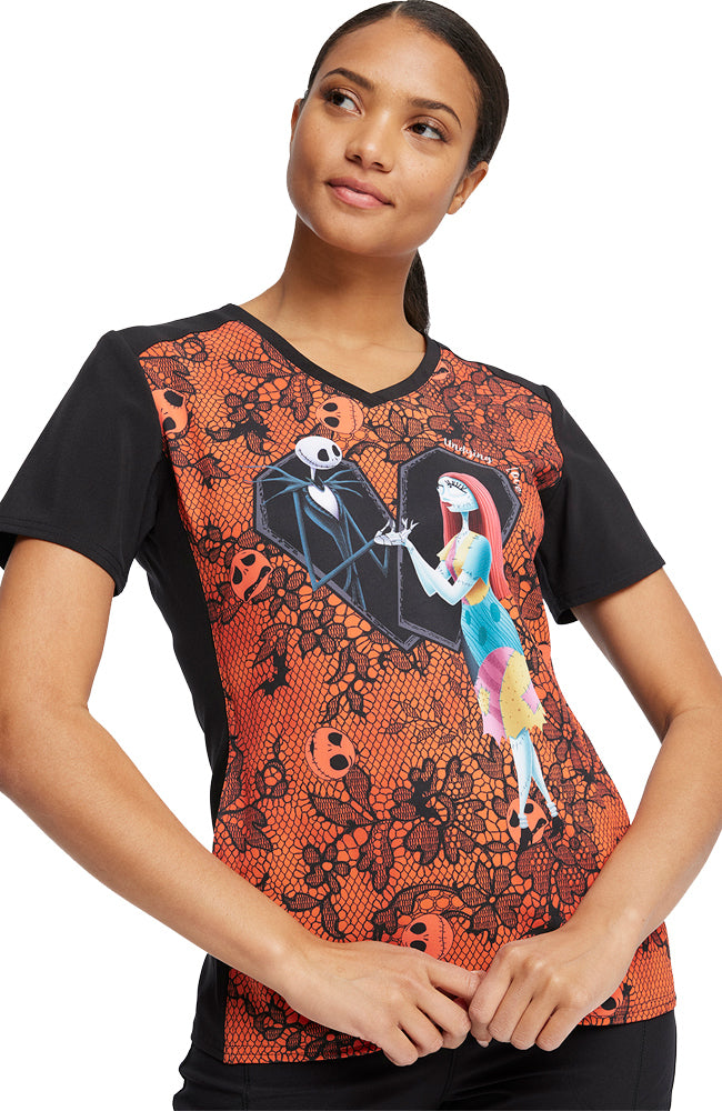 A young female Pediatric Nurse wearing a Tooniforms Women's V-Neck Printed Scrub Top in "Undying Love" featuring Jack Skellington and Sally from Tim Burton's "The Nightmare Before Christmas".
