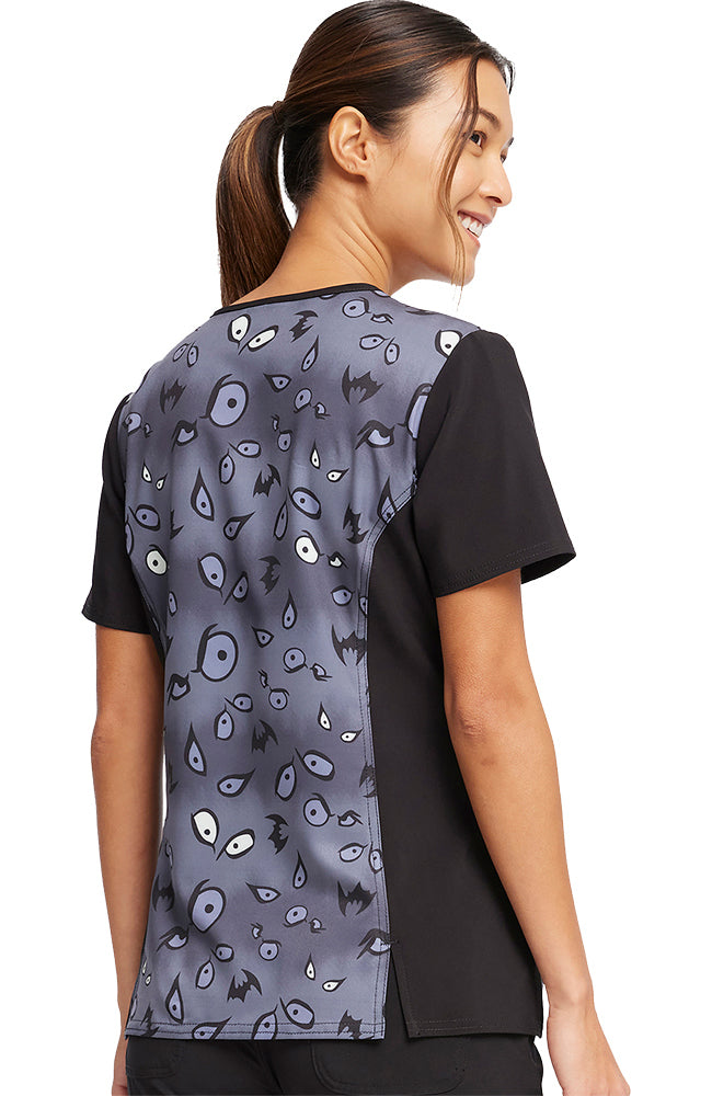 A young female Oncology Nurse wearing a Tooniforms Women's V-Neck Printed Scrub Top in "Under Wraps" size medium featuring a center back length of 25.5".