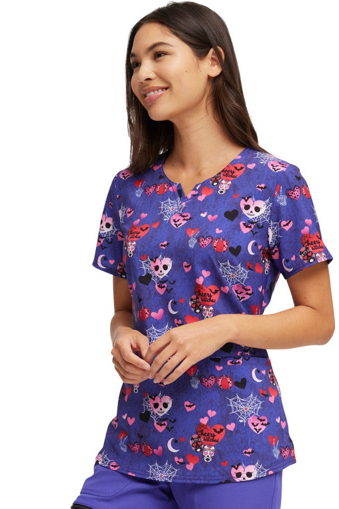 A young female Nurse wearing a HeartSoul Women's Halloween V-Neck Printed Scrub Top in "Cheers Witches" featuring a shirttail hem.