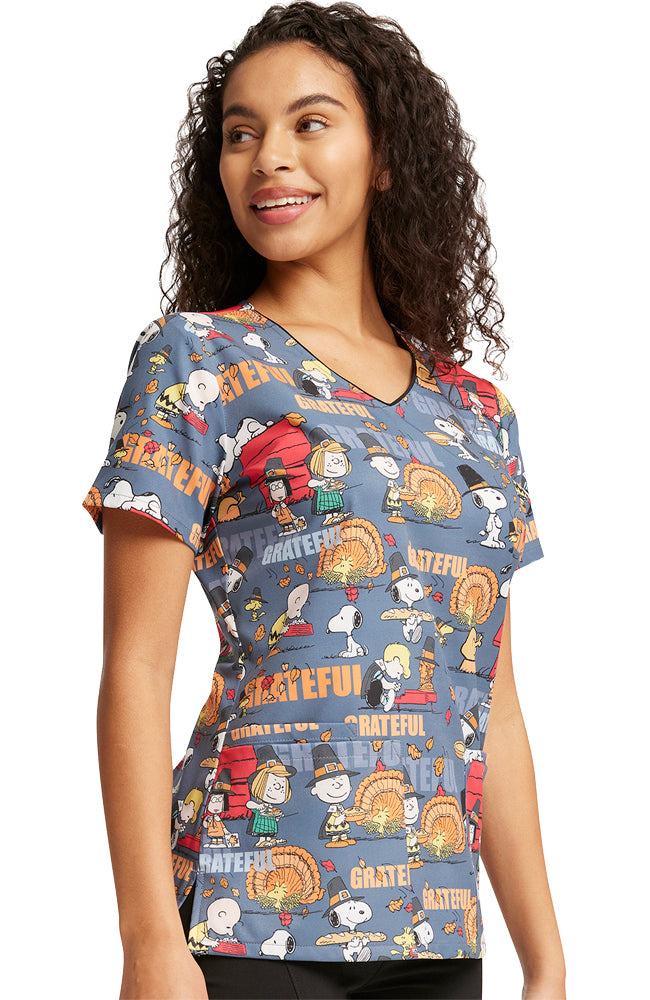 A young female Nurse wearing a Tooniforms Women's Thanksgiving Printed Scrub Top in "Grateful Snoopy" featuring side vents.