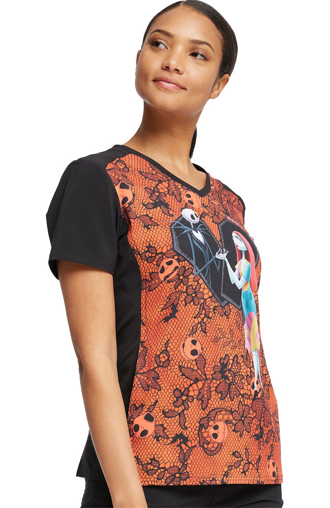 A young female Child Healthcare Specialist wearing a Tooniforms Women's Halloween V-Neck Printed Scrub Top in "Undying Love" featuring side contrast panels.