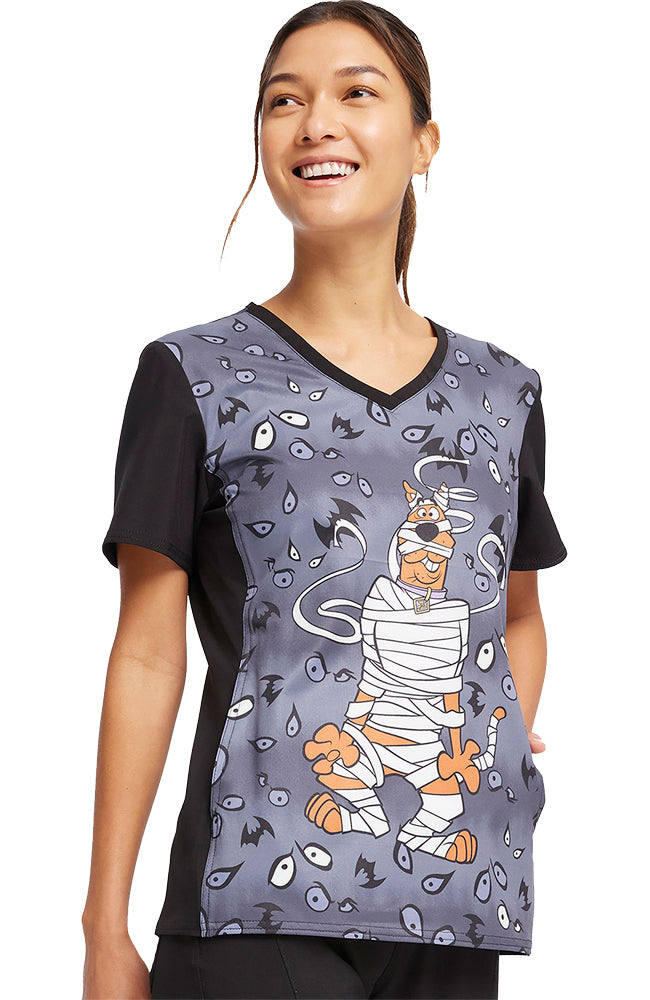 A young female Veterinarian wearing a Tooniforms Women's V-Neck Printed Scrub Top in "Under Wraps" size large featuring 1 front kangaroo pocket.