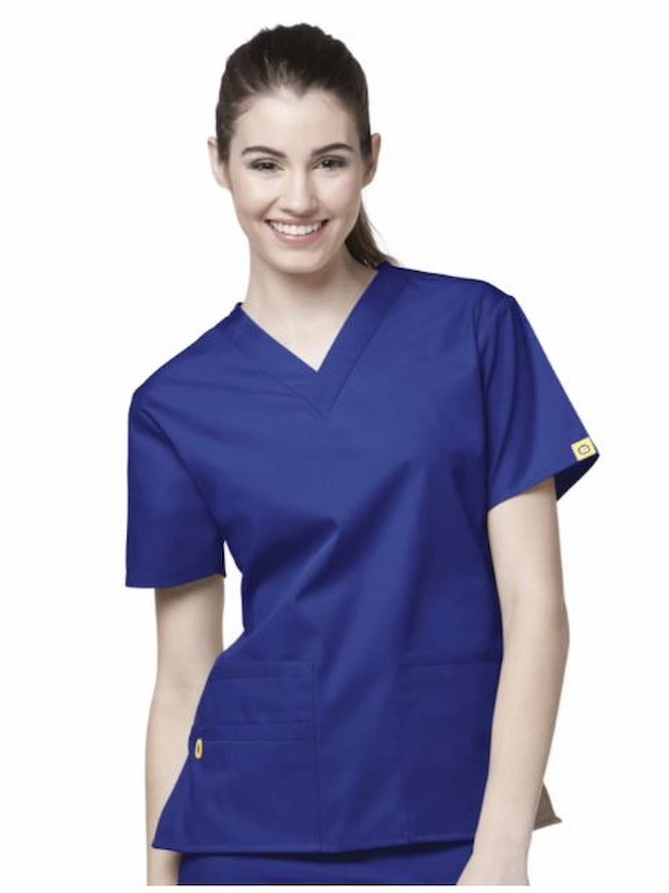 A young female nurse practitioner wearing a WonderWink Origins Women's Bravo V-neck Scrub Top in Galaxy Blue size Small featuring a soft poly cotton blend, 5 total pockets & short sleeves.