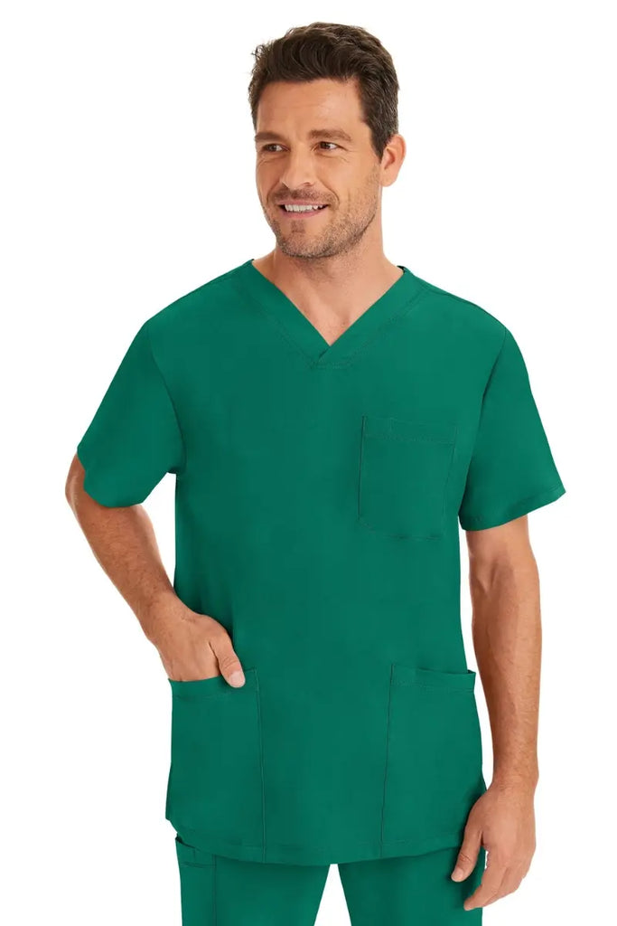 A male healthcare professional wearing an HH-Works Men's Matthew V-Neck Scrub Top in Hunter Green featuring a total of 4 pockets. for all your on the job storage needs.