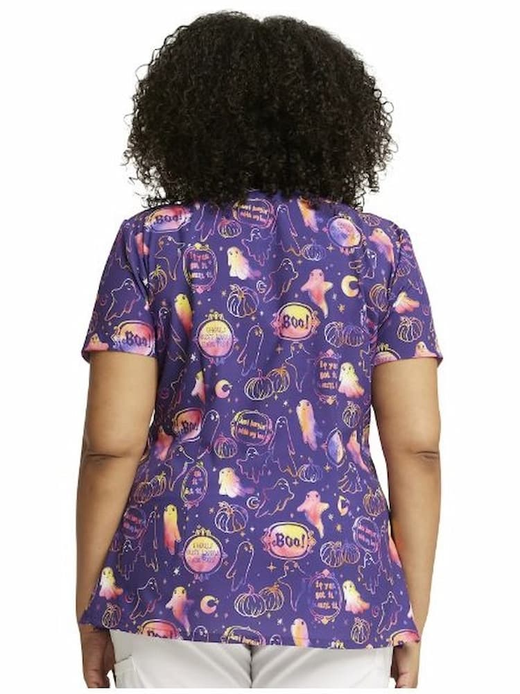 A young female Oncology Nurse wearing a Dickies WOmen's V-Neck Halloween Printed Scrub Top in "Hanging with My Boo" featuring a a center back length of 26".