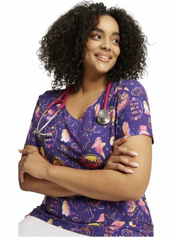 A young female Pediatric Nurse wearing a Dickies Women's V-Neck Halloween V-Neck Printed Scrub Top in "Hanging with My Boo" size 2XL featuring short sleeves.