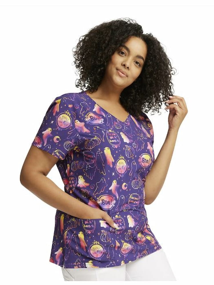 A young female Nurse Practitioner wearing a Dickies Women's V-Neck Halloween Printed Scrub Top in "Hangning with My Boo" featuring two front patch pockets and side slits.