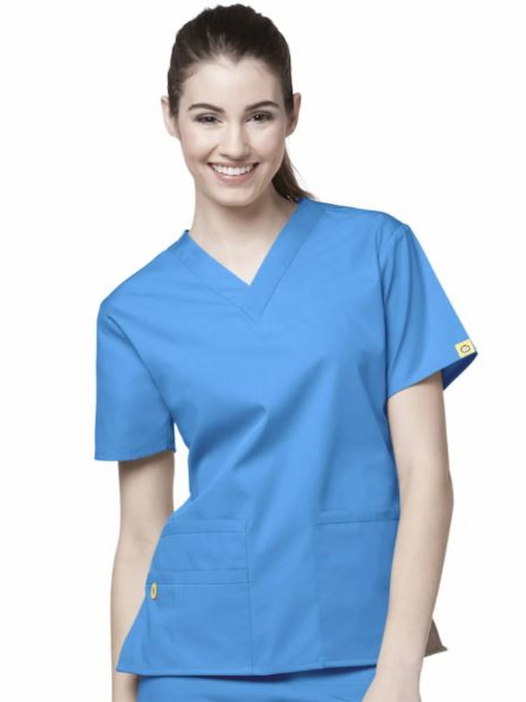 A young female medical assistant wearing a WonderWink Origins Women's Bravo V-neck Scrub Top in Malibu Blue size Medium featuring a total of 5 pockets.