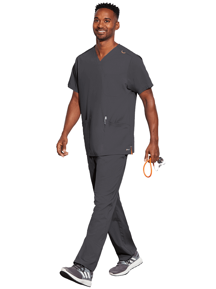 A young male CNA wearing a Barco Motion Unisex V-Neck Scrub Top in Pewter size Medium featuring 2 front patch pockets for all your on the job storage needs.
