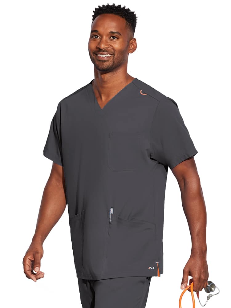 A young male Nurse wearing a Barco Motion Unisex V-neck Scrub Top in Pewter size Medium featuring a v-neckline with lap over styling.