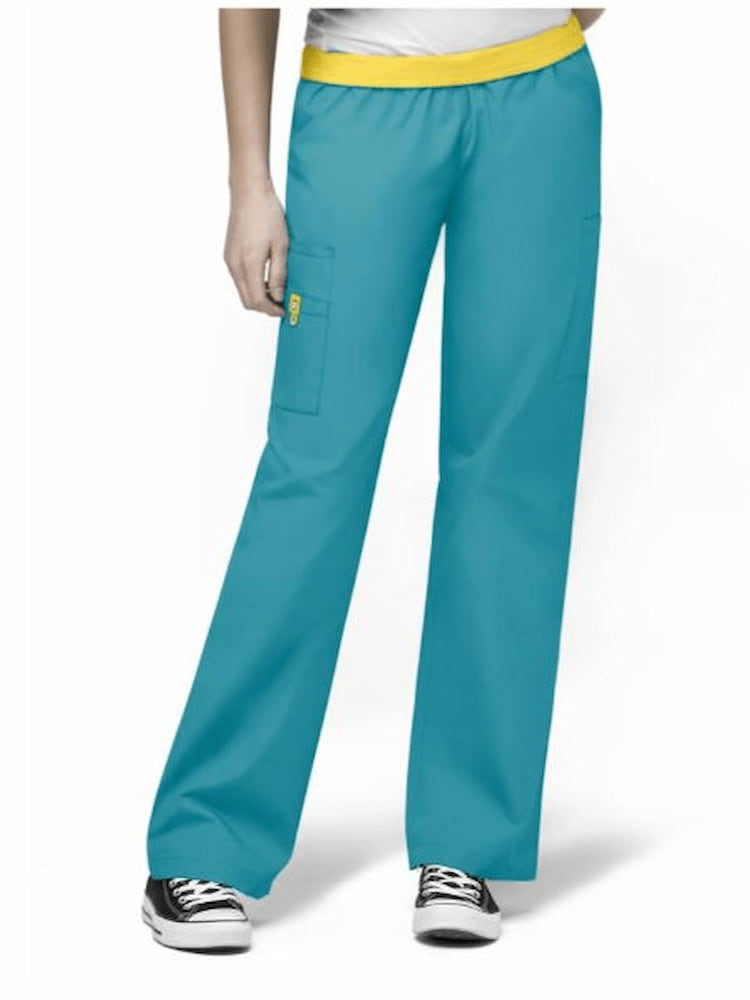 A young female Home Health Aide wearing a pair of WonderWink Women's Elastic Waist Quebec Scrub Pants in Real Teal size Small Tall featuring  one WonderWink signature triple pocket with hidden mesh cell phone pocket.
