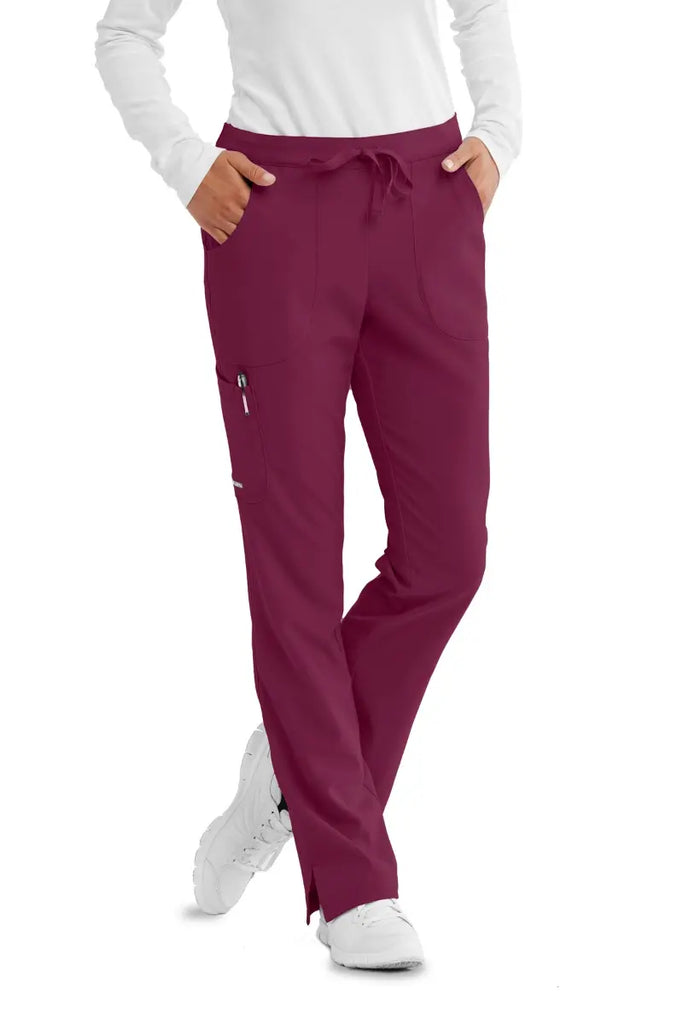 A young female nurse wearing a Skechers Women's Reliance Cargo Scrub Pants in Wine size XS featuring a junior contoured fit.