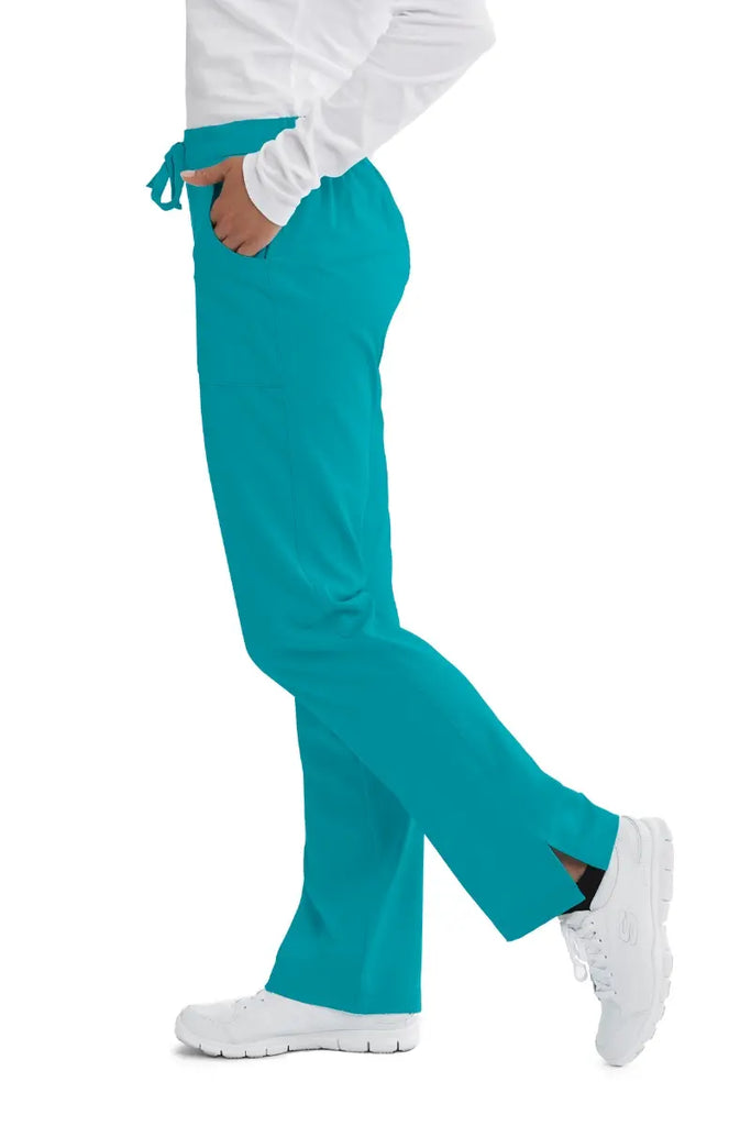 A young female nurse showcasing the left side of the Skechers Women's reliance Cargo Scrub Pant in Teal size XL featuring ankle vents at the hem.