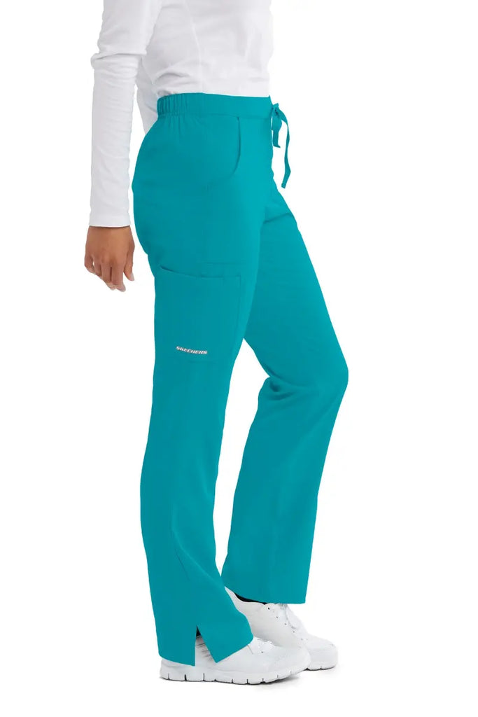 A close look at the right side of the Skechers Women's Reliance Caargo Scrub Pant in Teal size Medium featuring a side cargo pocket with the Skechers' logo printed on bottom of the pocket.