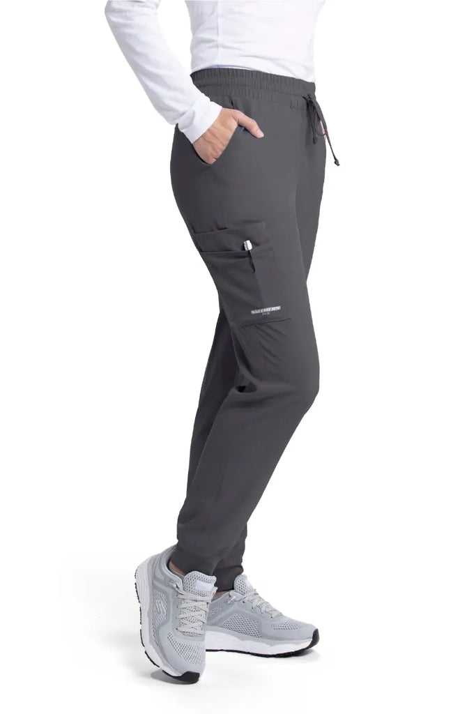 The Skechers Women's Theory Scrub Joggers in Pewter size small featuring an exterior cargo pocket on the wearer's right side leg.