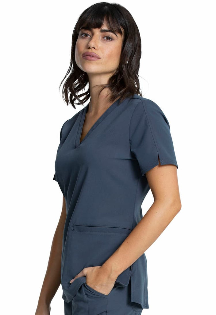 A female Surgical Assistant wearing a Vince Camuto Women's V-neck Scrub Top in Pewter size Large featuring side slits for additional mobility throughout the day.