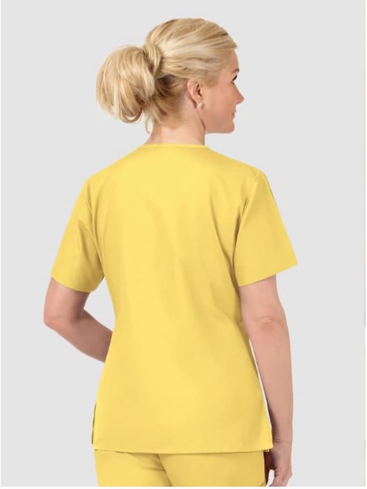 A middle aged female Nursing Assistant wearing a WonderWink Origins Women's Bravo Scrub Top in Yellow sixe XL featuring vented sides.