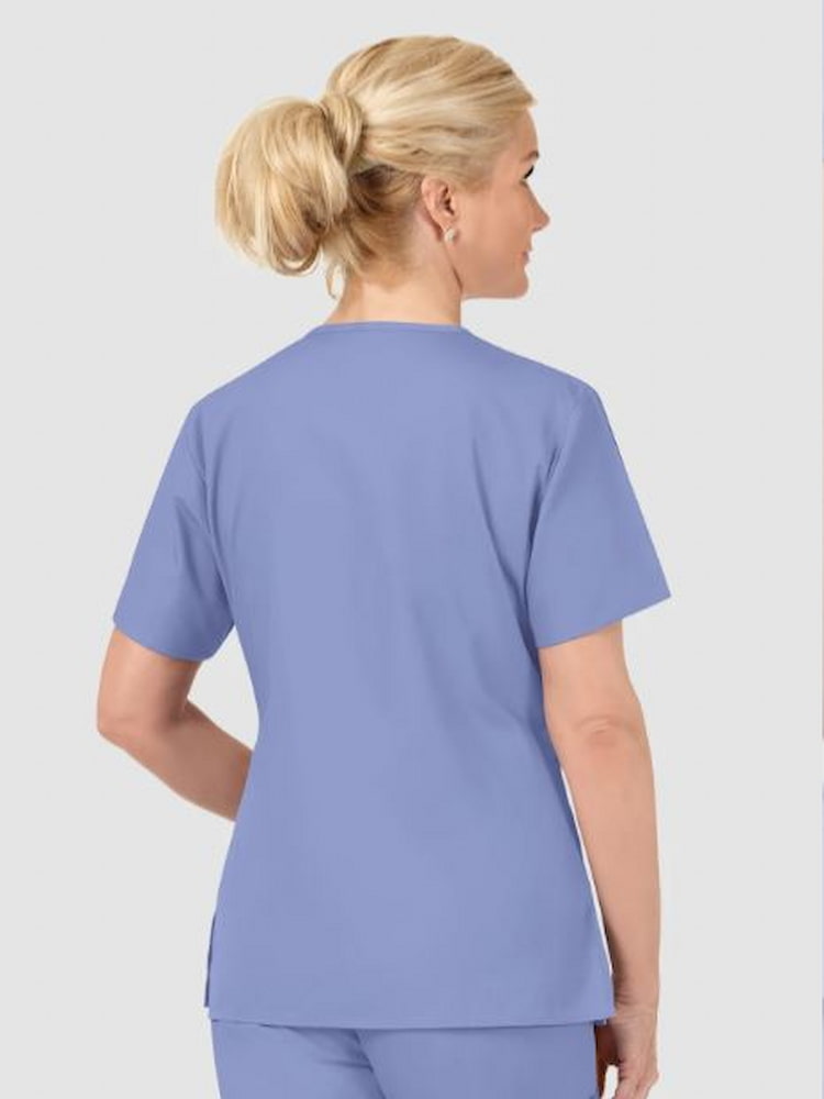 A middle aged female Nurse wearing a WonderWink Women's Bravo 5 Pocket Scrub Top in Ceil Blue size XL featuring side vents for additional mobility.