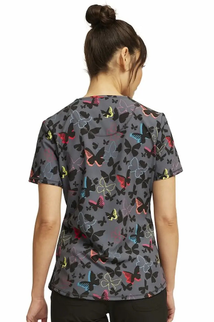 A young female Psychiatric Nurse wearing a Cherokee Infinity Women's Round Neck Printed Scrub Top in "Brilliant Butterflies" size Medium featuring a center back length of 25" for optimal coverage.
