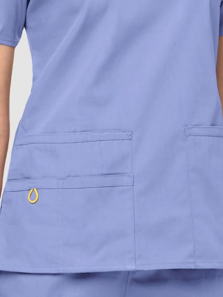 A close up image of the two lower front patch pockets on the WonderWink Origins Women's Bravo Scrub Top in Ceil Blue size XXS.