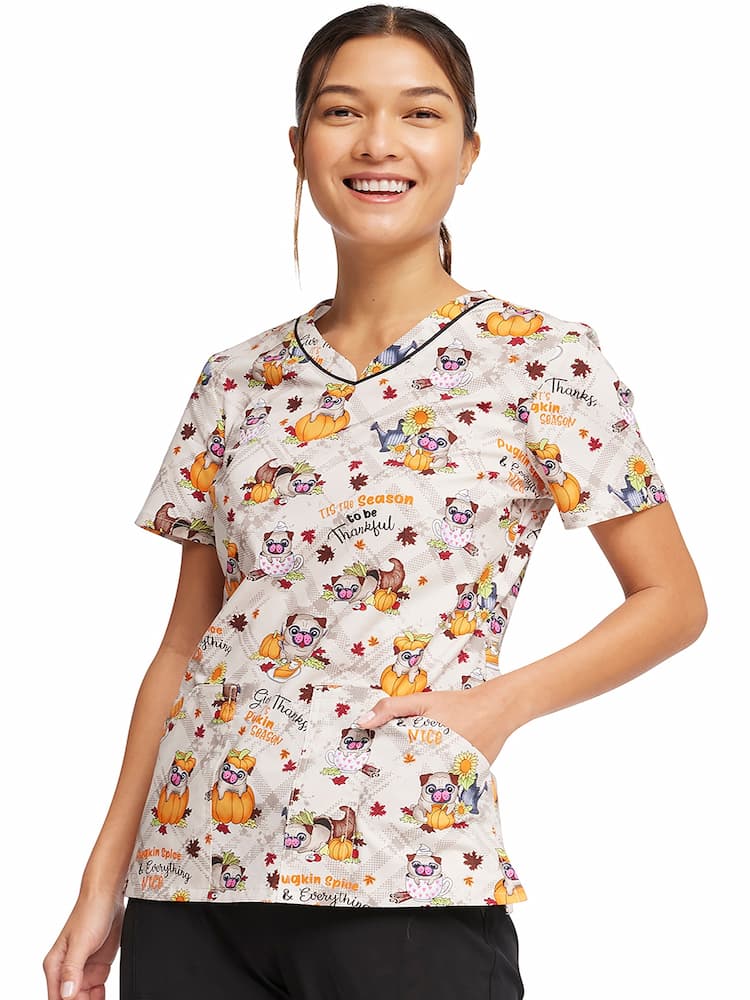 A young female Pediatric Nurse wearing a Cherokee Women's V-Neck Printed Scrub Top in "Pugkin Spice" size small featuring short sleeves.