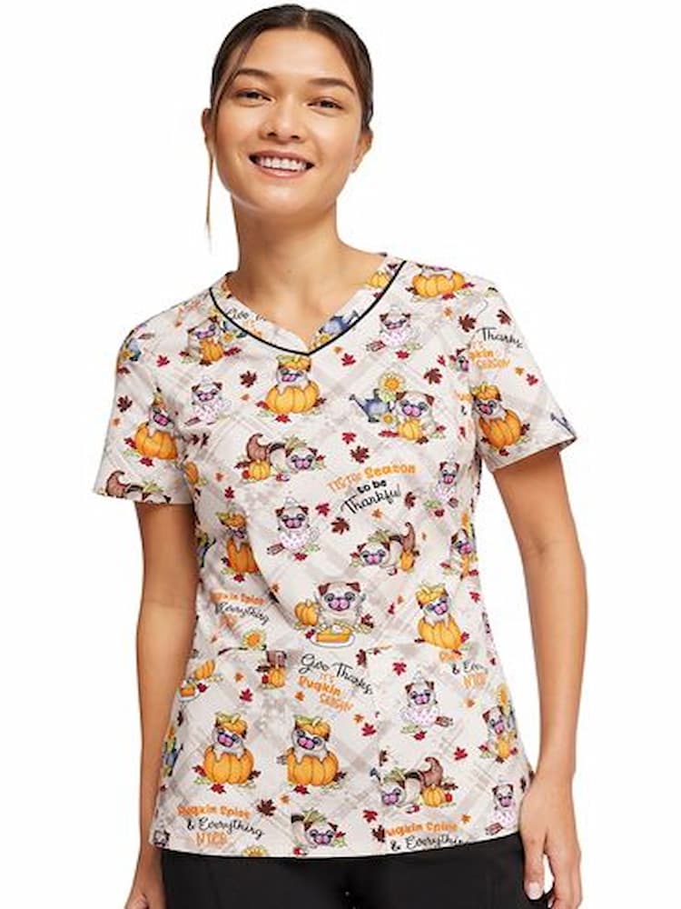 A young female Nurse Practitioner wearing a Cherokee Women's V-Neck Printed Scrub Top in "Pugkin Spice" darts at the bust for a flattering fit.
