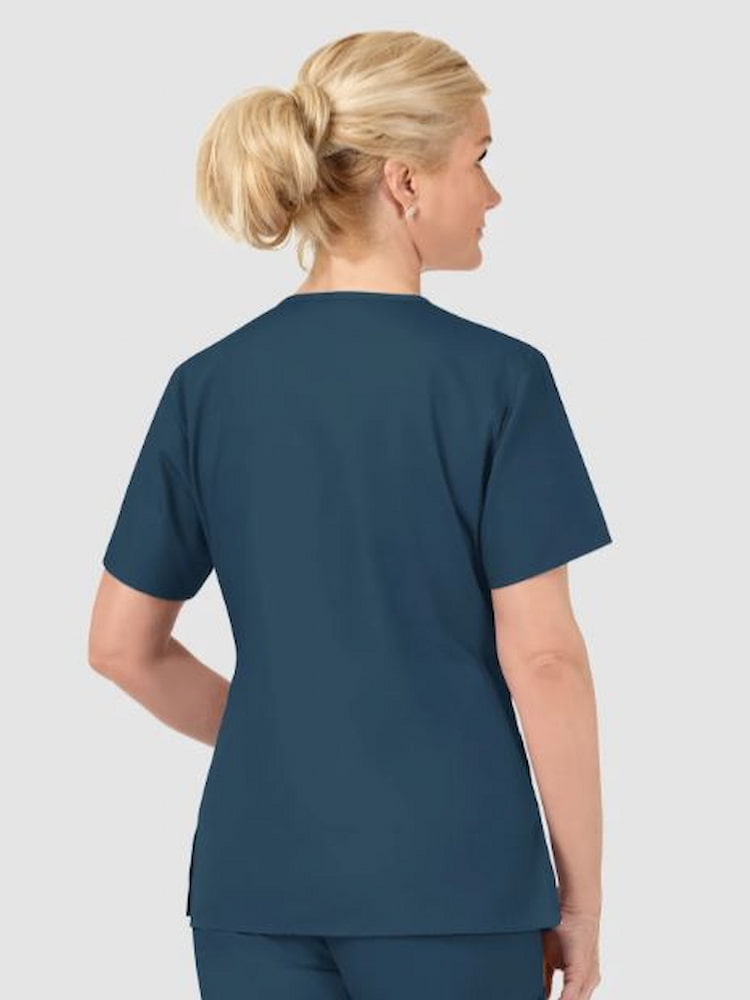 A middle aged female Registered Nurse wearing a WonderWink Origins Women's Bravo V-neck Scrub Top in Caribbean Blue featuring side vents to provide additional mobility.