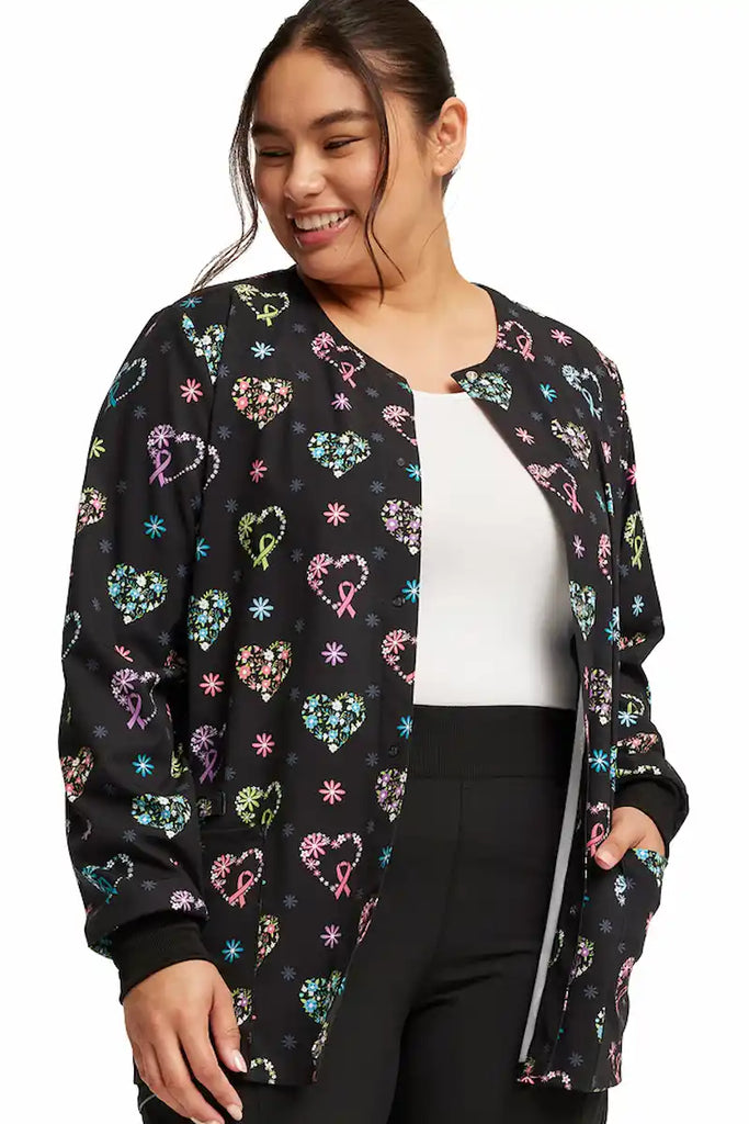 A young female Registered Nurse wearing a Cherokee Women's Print Front Snap Jacket in "Care Flor-All" size large featuring 2 front patch pockets.