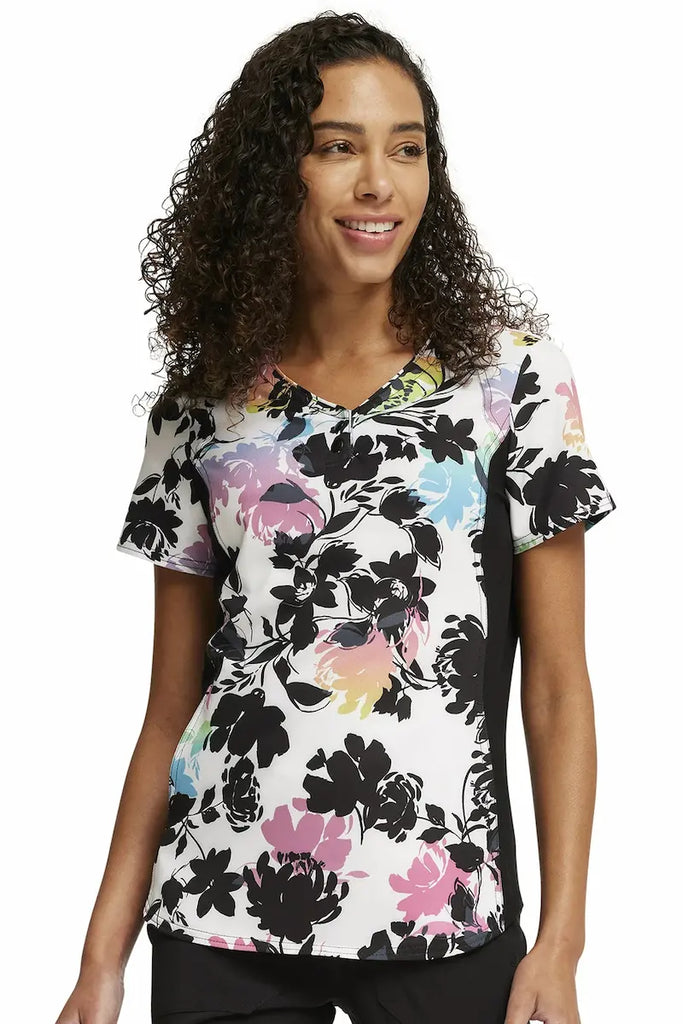 A young female Cherokee iFlex Women's V-neck Print Scrub Top in "Garden Glow" size Small featuring a modern classic fit.