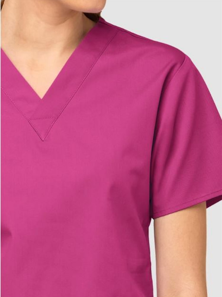 An up close image of the v-neckline on the WonderWink Origins Women's Bravo Scrub Top in Hot Pink size Medium featuring short sleeves.