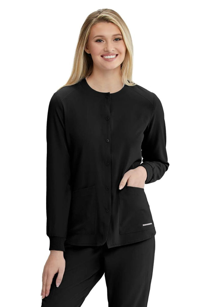 A female Phlebotomist wearing a Skechers women's Stability Snap Front Scrub Jacket in black size 2XL featuring a center front snap closure.