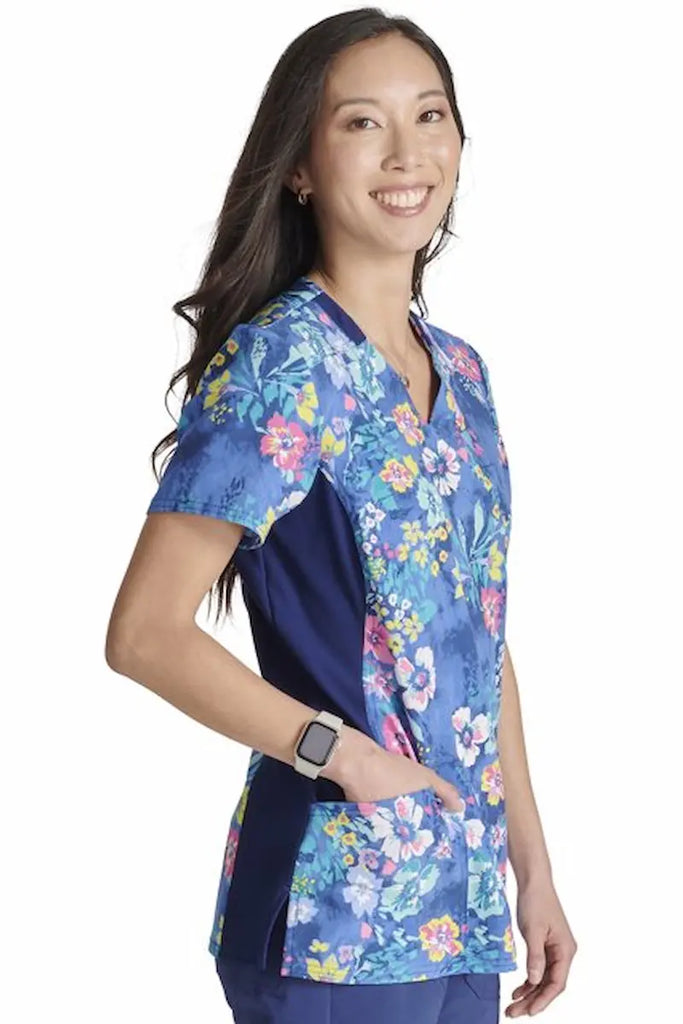 A young female Labor and Delivery Nurse wearing a Cherokee Women's Knit Panel Printed Scrub Top in "Blooming Tie Dye" size 2XL featuring side slits for additional range of motion.