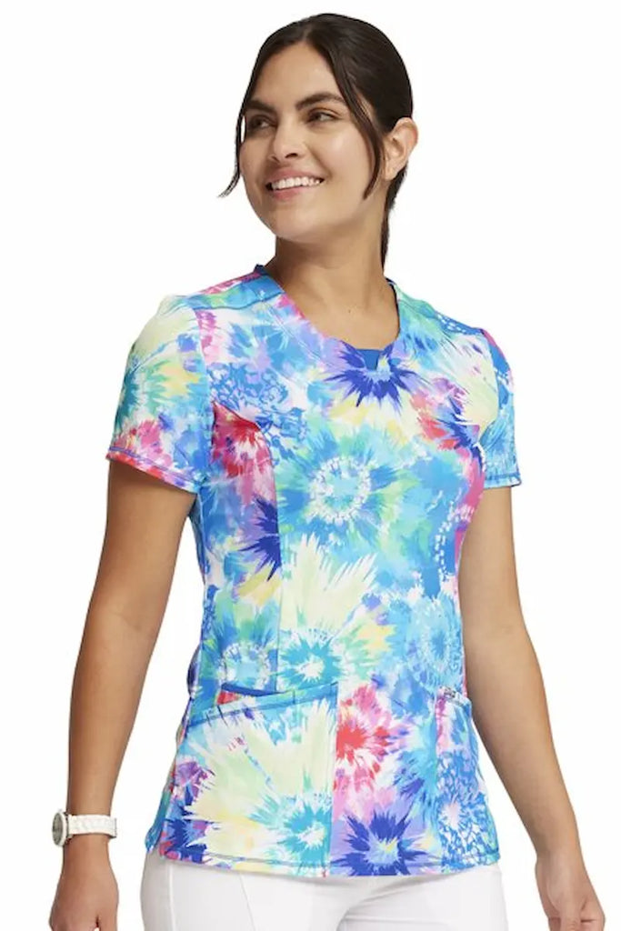 A young female Neonatal Nurse wearing a Cherokee Infinity Women's Round Neck Printed Scrub Top in "Tie Dye Burst" size XS featuring a soft and breathable fabric made of 95% polyester and 5% spandex.