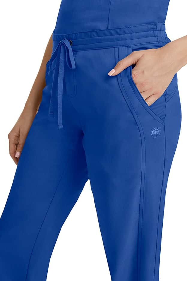 A young woman wearing a pair of Purple Label Women's Taylor Drawstring Scrub Pants from Healing Hands in Galaxy Blue. Perfect for Healthcare Professionals working in Hospitals, Doctors offices, Dental Groups & Veterinary offices!