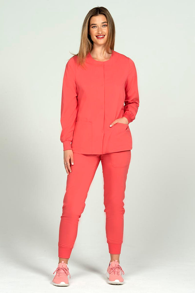 A female nurse wearing an Epic by MedWorks Women's Snap Front Scrub Jacket in Coral size XL featuring a super soft, easy care fabric designed to keep you looking and feeling great all day.