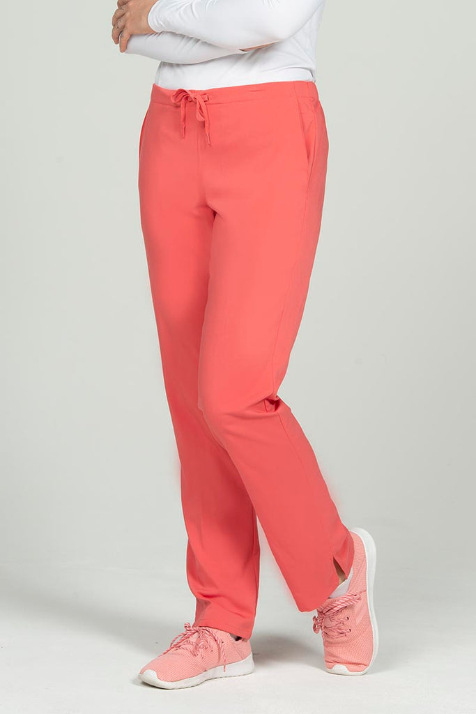 A young female Pharmacy Technician wearing an Epic by MedWorks Natural Rise Flare Leg Scrub Pant in Coral size small featuring a unique stretch fabric made of 77% Polyester, 21% Viscose, 2% Spandex.