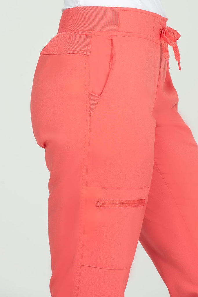 A young female Nurse Anesthetist wearing nan Epic by MedWorks Women's Skinny Yoga Scrub Pant in Coral size Medium Petite featuring a total of 3 pockets.