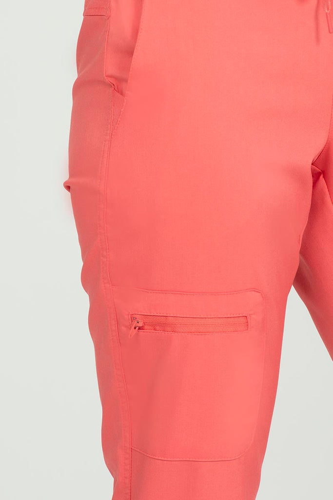 A young female Nurse wearing an Epic by MedWorks Women's Skinny Yoga Scrub Pant in Coral size 2XL featuring 1 zip closure cargo pocket on the wearer's right side.