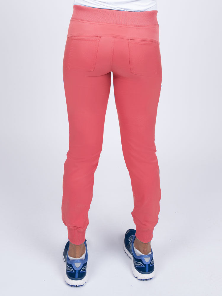 A young female Nurse Practitioner wearing an Epic by MedWorks Women's Yoga Jogger Scrub Pant in Coral size small featuring 2 back patch pockets.