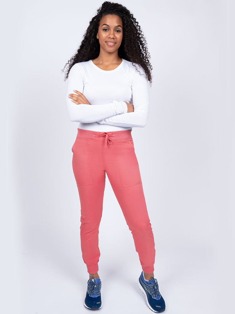 A young lady nurse wearing an Epic by MedWorks Women's Yoga Jogger Scrub Pant in Coral size Large Petite featuring stylish cover stitch detail throughout.