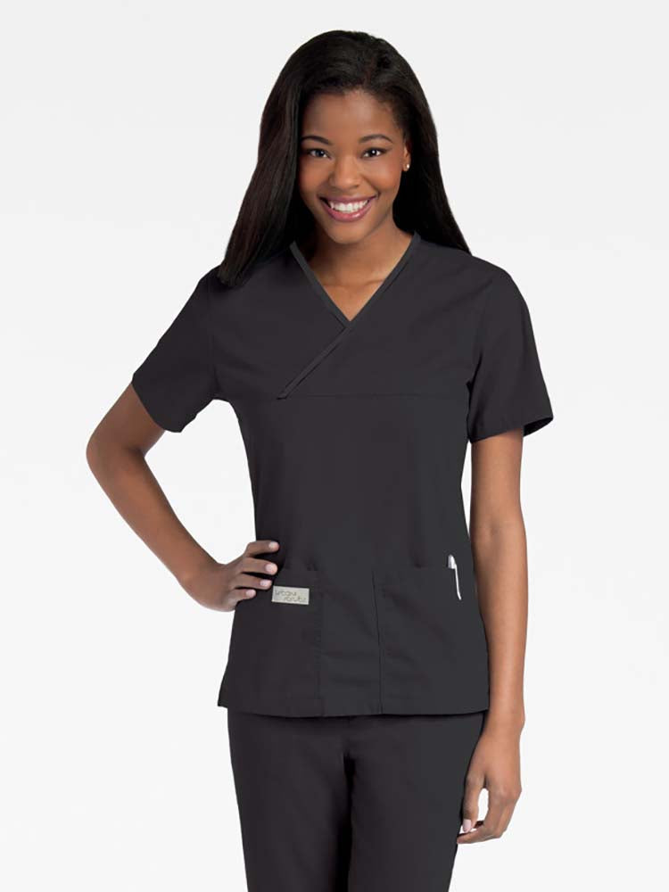 Young lady wearing an Urbane Essentials Women's Crossover Scrub Top in "Black" featuring a unique crossover neckline for a flattering fit.