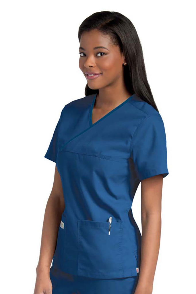 Female nurse wearing an Urbane Essentials Women's Crossover Scrub Top in "Royal Blue" featuring 2 front patch pockets.