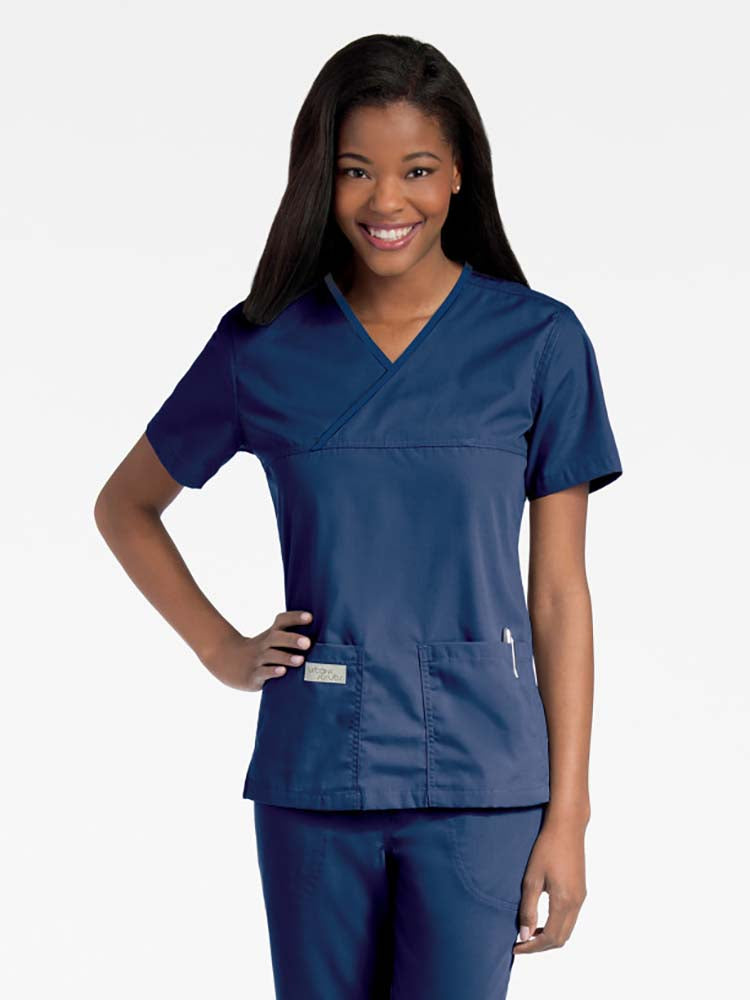 Young lady wearing an Urbane Essentials Women's Crossover Scrub Top in "Navy" featuring a unique crossover neckline for a flattering fit. 