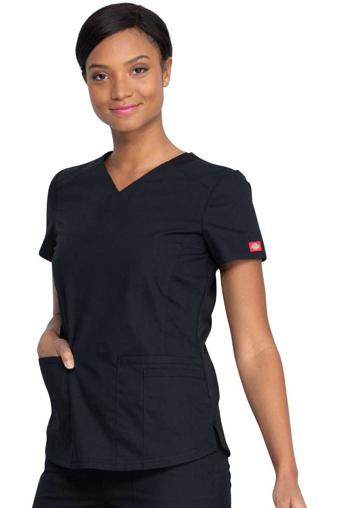 A young female LPN wearing a Dickies EDS Signature Women's V-neck Scrub Top in Black size Large featuring princess seaming throughout the front.