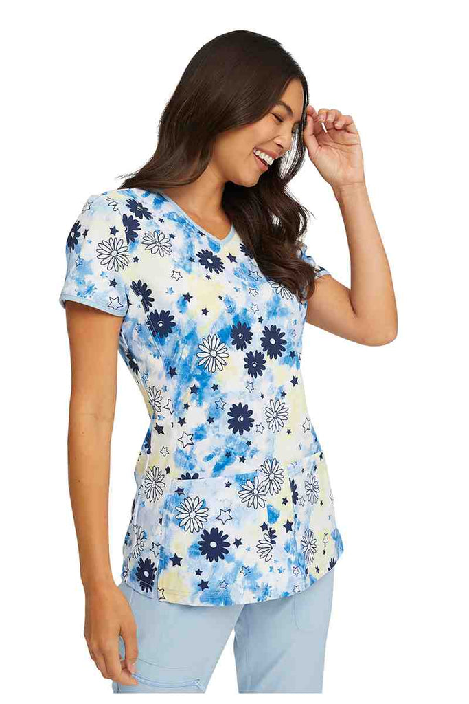 A young female LPN wearing a HeartSoul Women's V-neck Print Scrub Top in "Daisy Spirit" size XL featuring a princess seaming throughout for shaping.