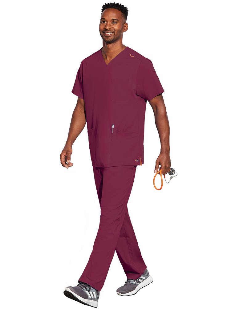 Young male LPN wearing a Unisex V-Neck Scrub Top in Wine size XL from Barco Motion featuring a total of 5 pockets for all of your daily storage needs.