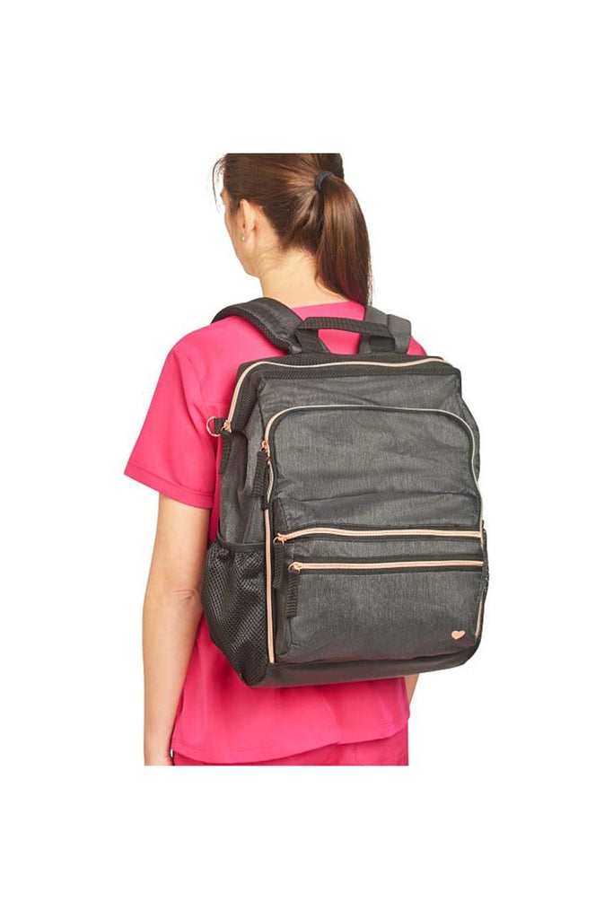 A young female Registered Nurse wearing a Nurse Mates Ultimate Backpack in "Charcoal\Rose Gold" featuring a variety of pockets & compartments to fit everything from laptops, medical supplies & more.
