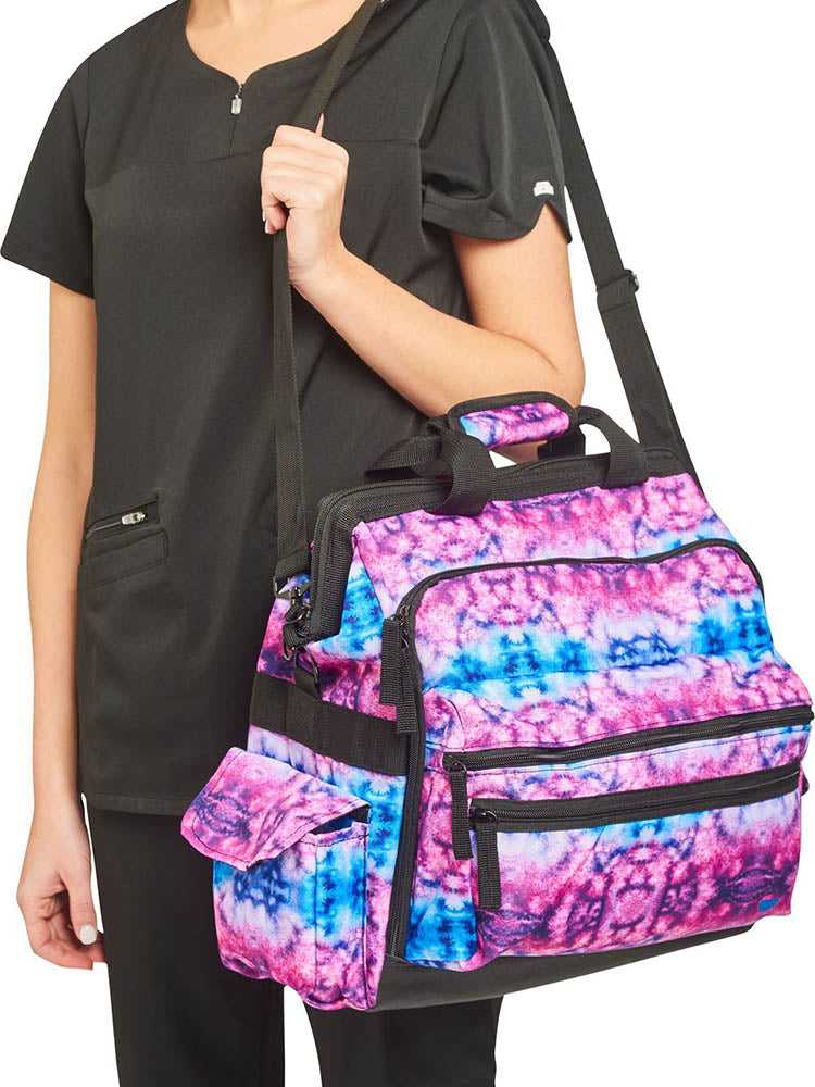 A young female Home Care Registered Nurse carrying a Nurse Mates Ultimate Medical Bag in "Berry Blue Tie Dye" featuring an adjustable nylon strap.