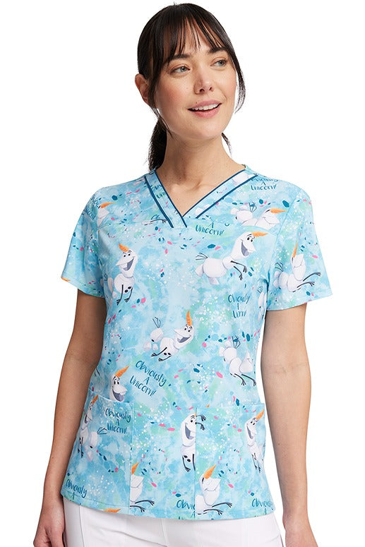 A young female nurse wearing a Women's V-Neck Print Scrub Top from Cherokee Tooniforms in "Obviously a Unicorn" featuring a modern classic fit.